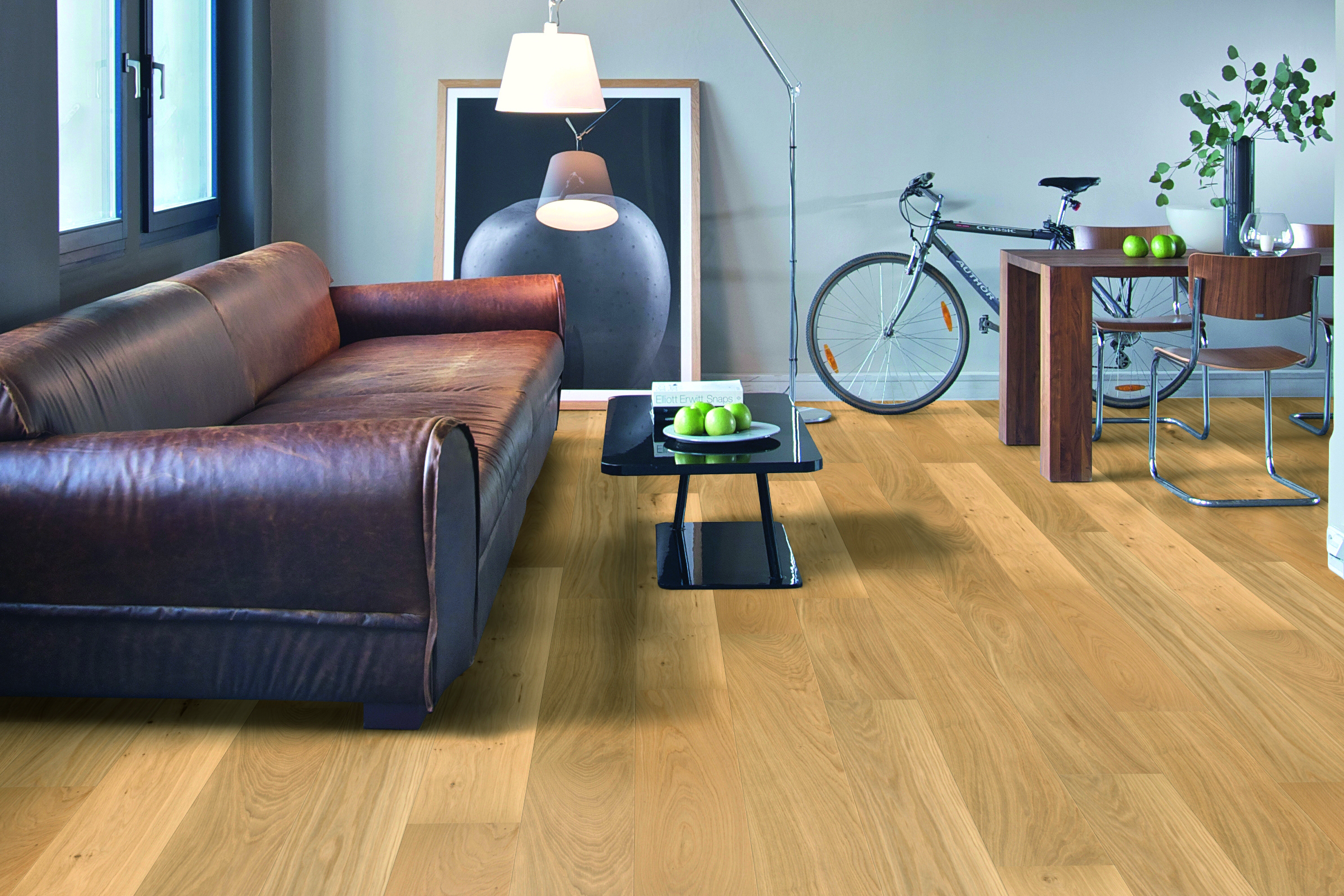 Modern living room featuring Nature's Oak engineered timber flooring, leather sofa, minimalist decor, glass coffee table with green apples, and bicycle in the background.