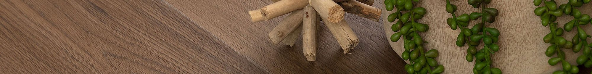 Anchor Grey flooring from the Corsica Collection, featuring natural wood texture and decorative plant elements.